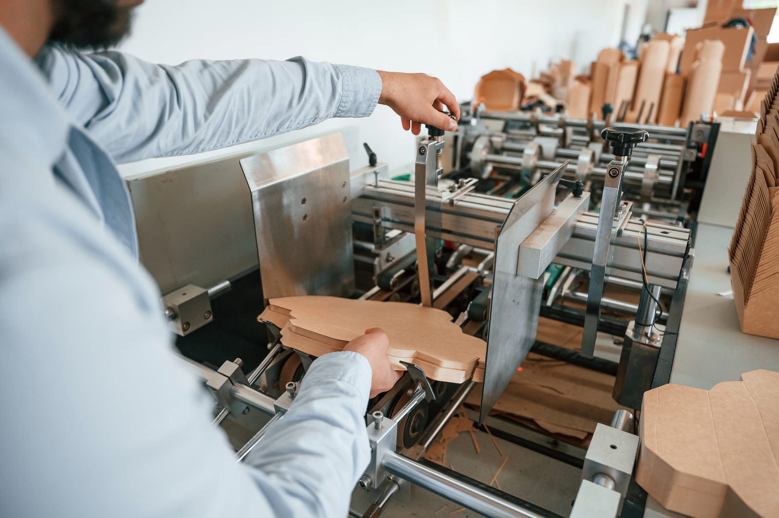 Operator running folded kraft boxes through an automated folder-gluer machine